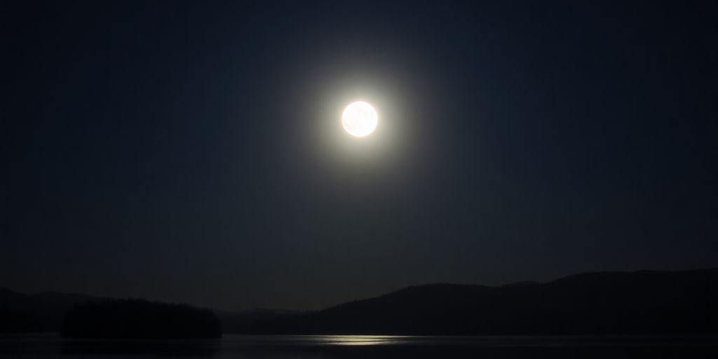 Voller Mond über ruhiger Landschaft mit Wasserreflexion.