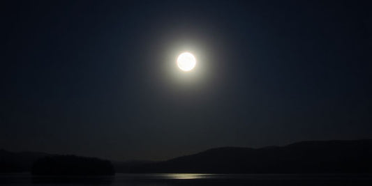 Voller Mond über ruhiger Landschaft mit Wasserreflexion.